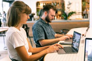 Mann und Frau sitzen jeweils vor einem Laptop und arbeiten an Designs